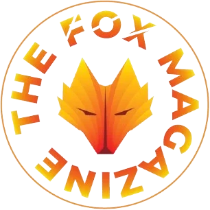 Logo of an orange foxhead encircled by the words 'THE FOX MAGAZINE' in an orange bottom to yellow top gradient sans-serif font in all caps inside an orange thin line circle. The word 'FOX' directly above the foxhead, has a transparent slash through each letter.